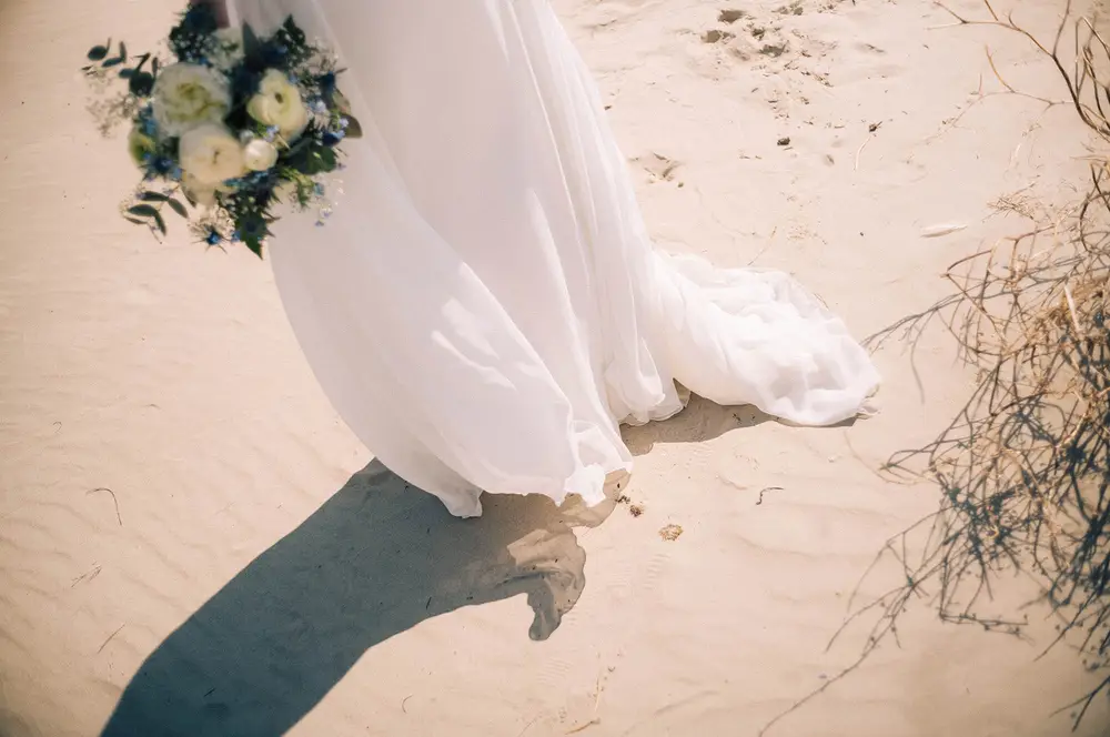 Wedding photo shoot in St. Peter-Ording on the beach, in the dunes. Elegant wedding dress blowing in the wind.