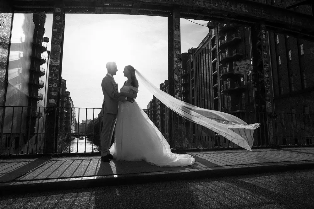 Wedding photography Hamburg Speicherstadt, Fleetschlösschen, Wasserschloss, Elbschlösschen, Elbschloss. Couple in backlight. Long bridal veil blowing in the wind. Leica M11.